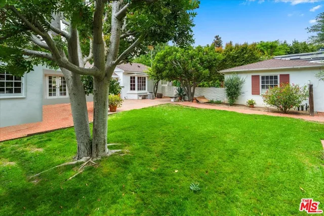 a backyard of a house with table and chairs plants and large tree