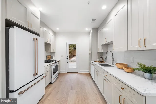 a large kitchen with stainless steel appliances sink a refrigerator and white cabinets