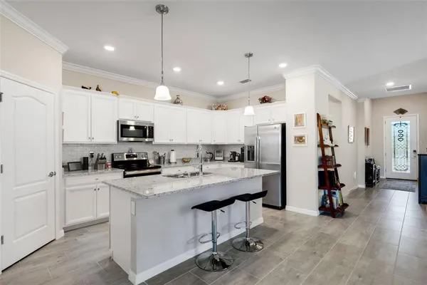 a kitchen with stainless steel appliances kitchen island granite countertop a stove a sink a refrigerator and white cabinets with wooden floor