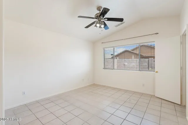 an empty room with chandelier fan and kitchen view