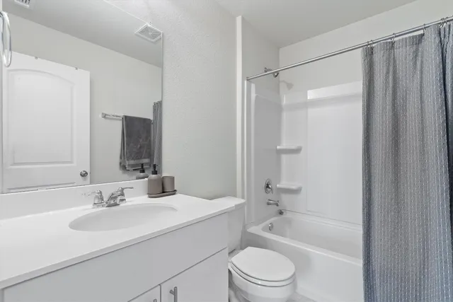 a bathroom with a granite countertop bathtub shower sink vanity mirror and toilet