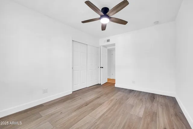 an empty room with wooden floor and a ceiling fan