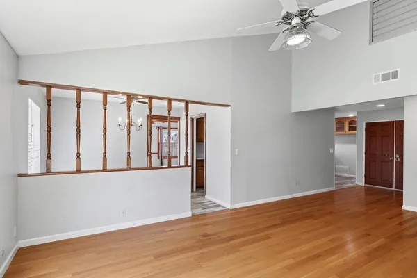 a view of an empty room with wooden floor and a ceiling fan
