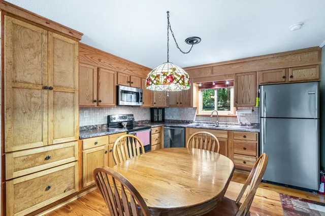 a kitchen with stainless steel appliances granite countertop a stove top oven a refrigerator a dining table and chairs with wooden floor