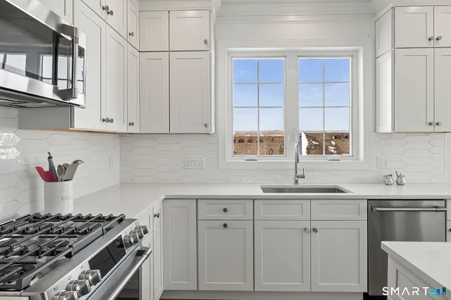 a kitchen with stainless steel appliances granite countertop white cabinets a sink a stove and a refrigerator