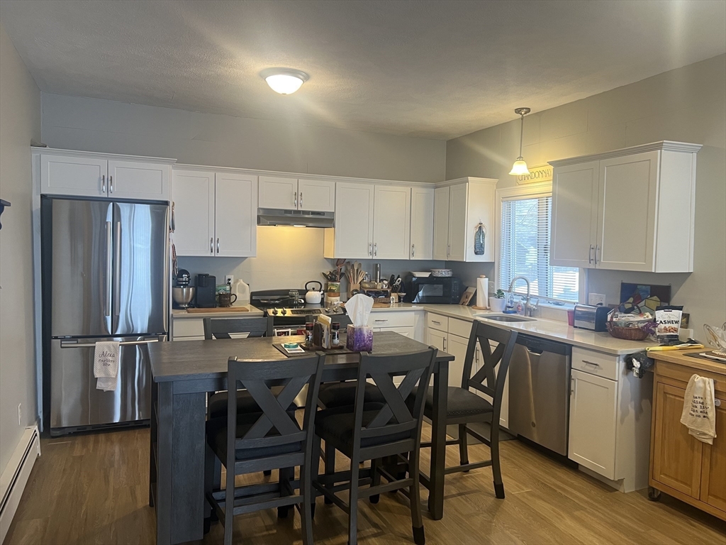 50 Humphrey Street, Unit 1 Swampscott, MA 01907 - Photo 2 of 12 a kitchen with a dining table chairs refrigerator and cabinets