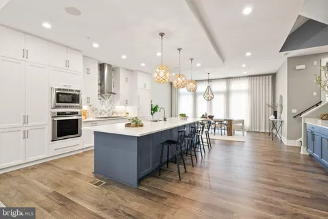 a room with stainless steel appliances kitchen island granite countertop a stove a sink a refrigerator and a dining table with wooden floor