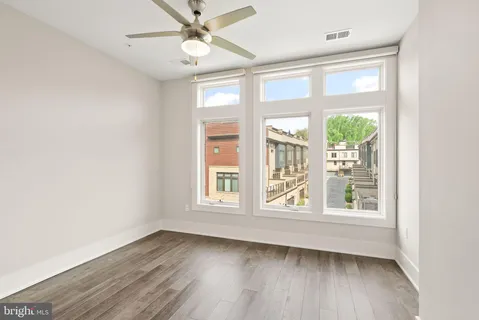 an empty room with wooden floor fan and windows