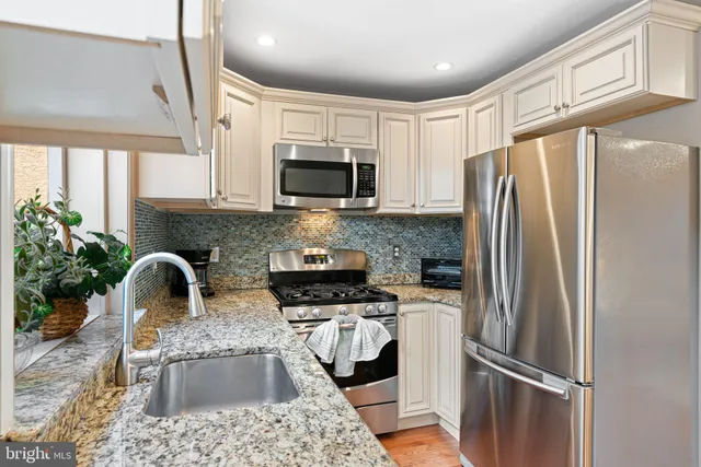 a kitchen with stainless steel appliances granite countertop a refrigerator a stove a sink a microwave a refrigerator and white cabinets