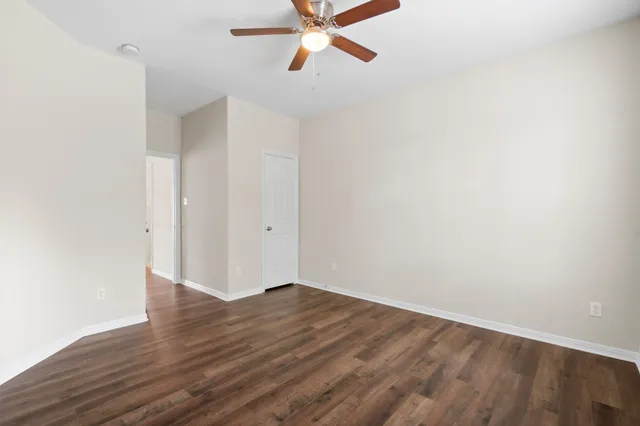 a view of an empty room with wooden floor and a ceiling fan