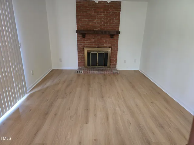 an empty room with wooden floor a fireplace and windows
