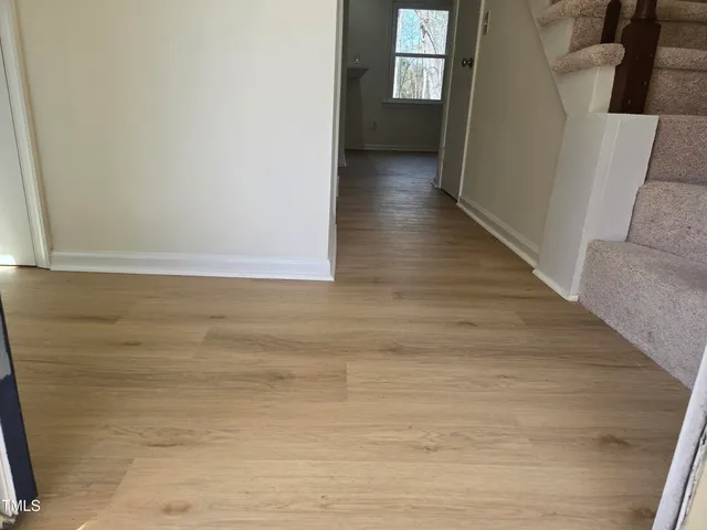 a view of a hallway to an empty room with wooden floor and a window