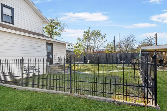 a view of a white house with a large tree and wooden fence