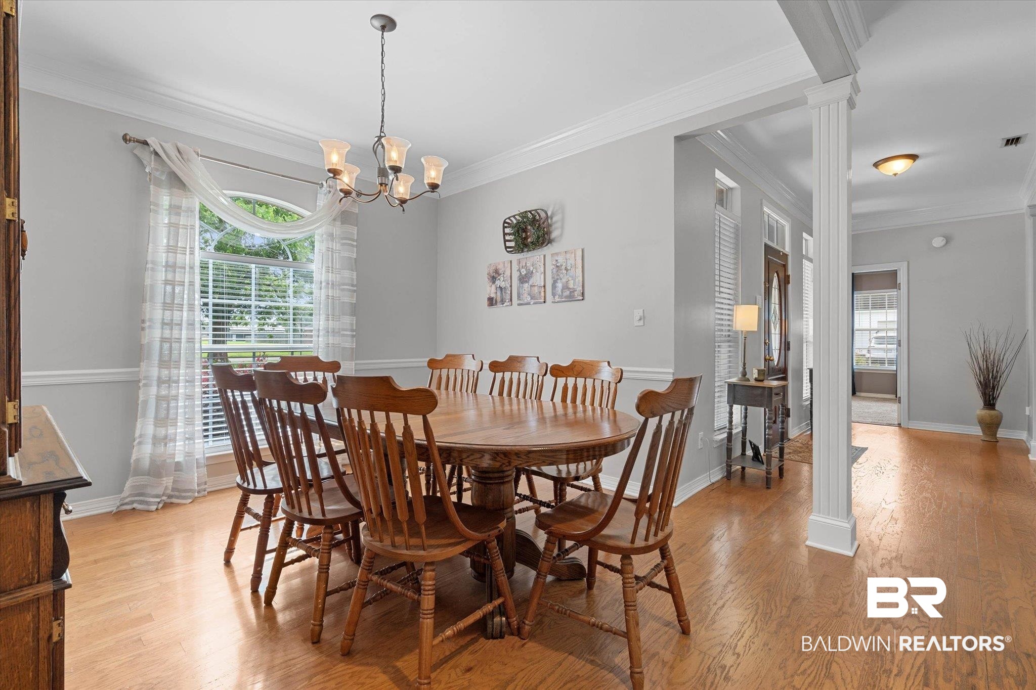3170 Scott Dairy Loop Road West Mobile, AL 36695 - Photo 5 of 24 Dining area featuring wood-finish flooring, a multi-light chandelier, a large window with blinds, decorative wall molding, and white interior columns