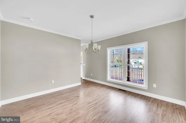 a view of an empty room with wooden floor and fan