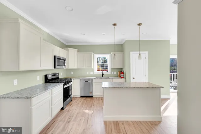 a kitchen with stainless steel appliances white cabinets a sink a stove a refrigerator and island with wooden floor