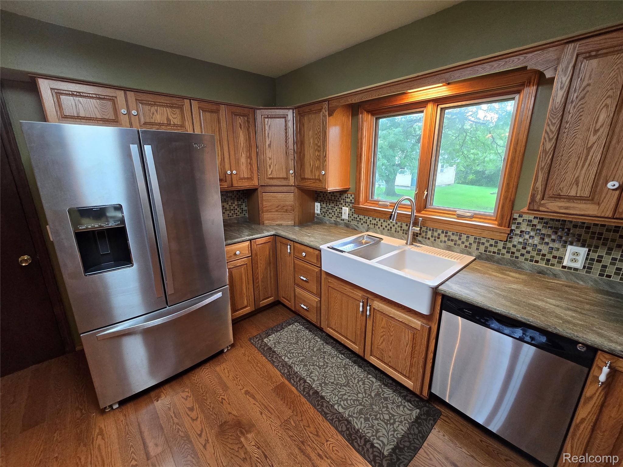 5282 McIntyre Road North Street, MI 48049 - Photo 19 of 53 Wood-finish flooring, custom wood cabinetry, stainless steel appliances, mosaic tile backsplash, and a double basin farmhouse sink