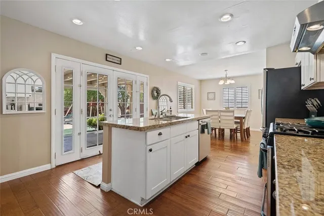 a kitchen with stainless steel appliances granite countertop a refrigerator a stove a sink dishwasher and a dining table with wooden floor