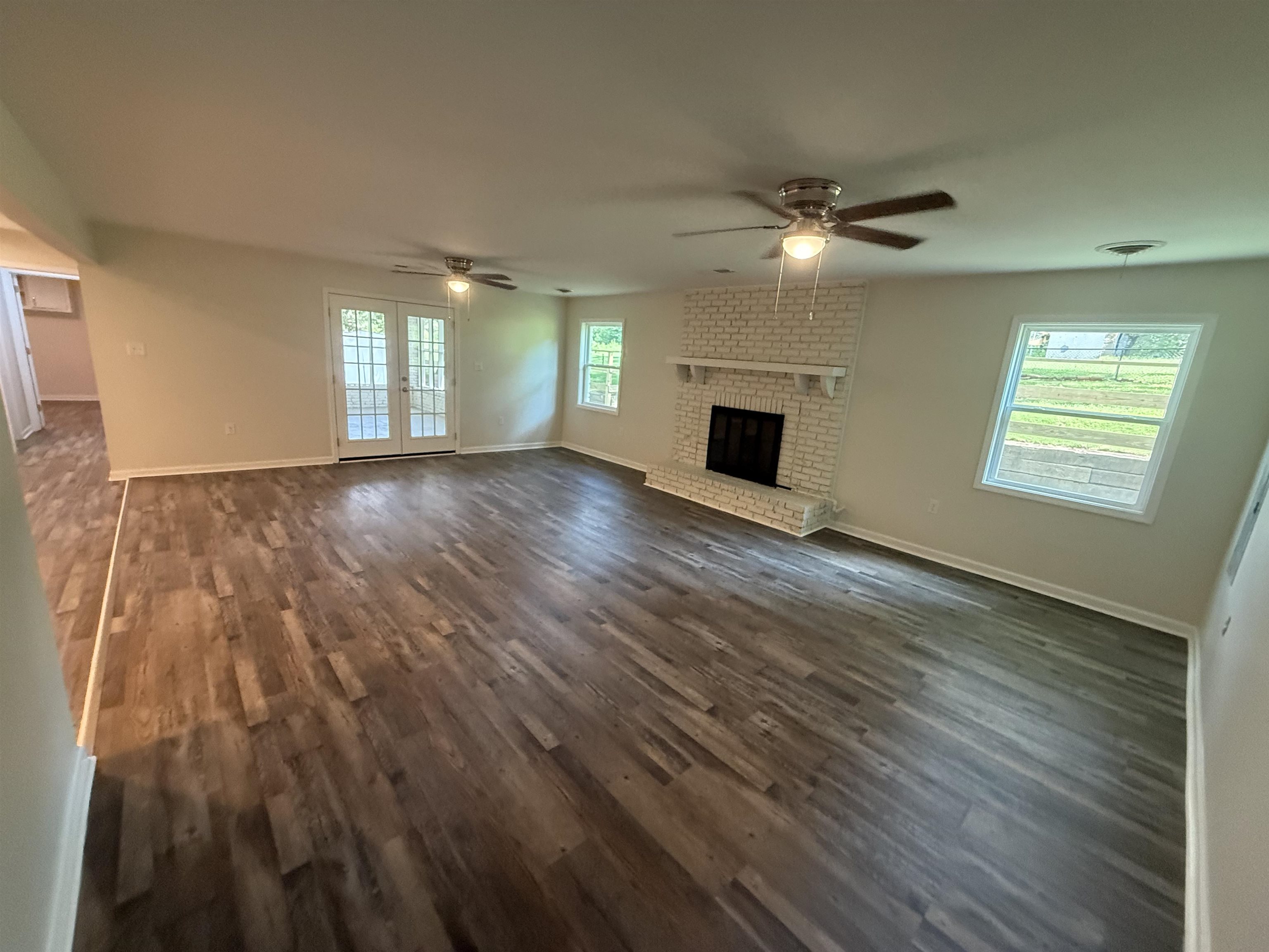 Spacious room featuring wood-finish flooring, a white brick fireplace with mantel, and two windows