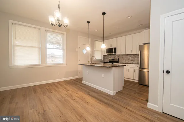 a kitchen with stainless steel appliances granite countertop a refrigerator a sink dishwasher a stove and white cabinets with wooden floor