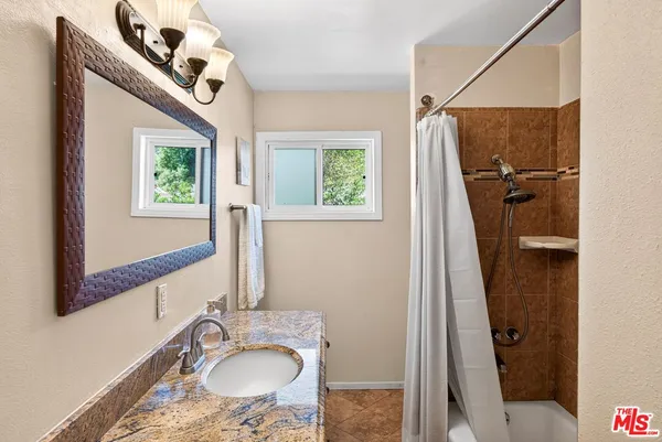 a bathroom with a granite countertop sink a mirror and shower