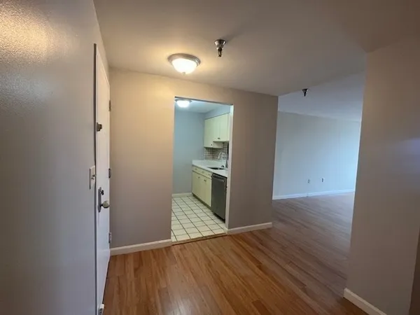 an empty room with wooden floor and a kitchen