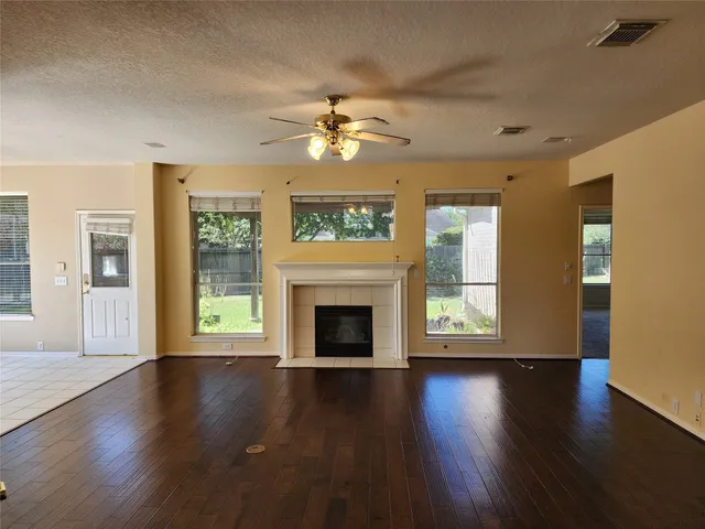 an empty room with wooden floor fireplace fan and windows