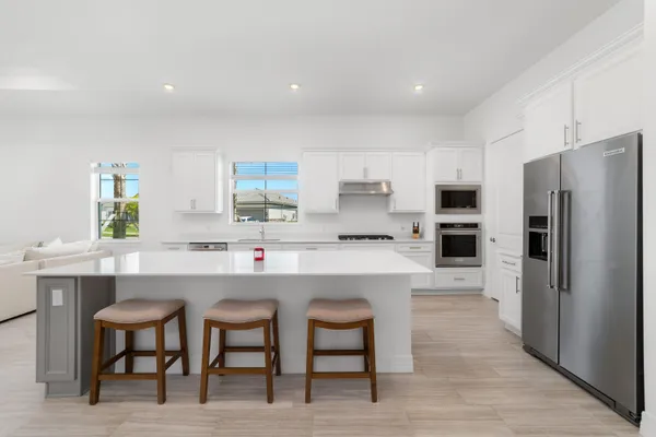 a kitchen with stainless steel appliances kitchen island granite countertop a dining table chairs and a refrigerator a sink dishwasher with wooden floor