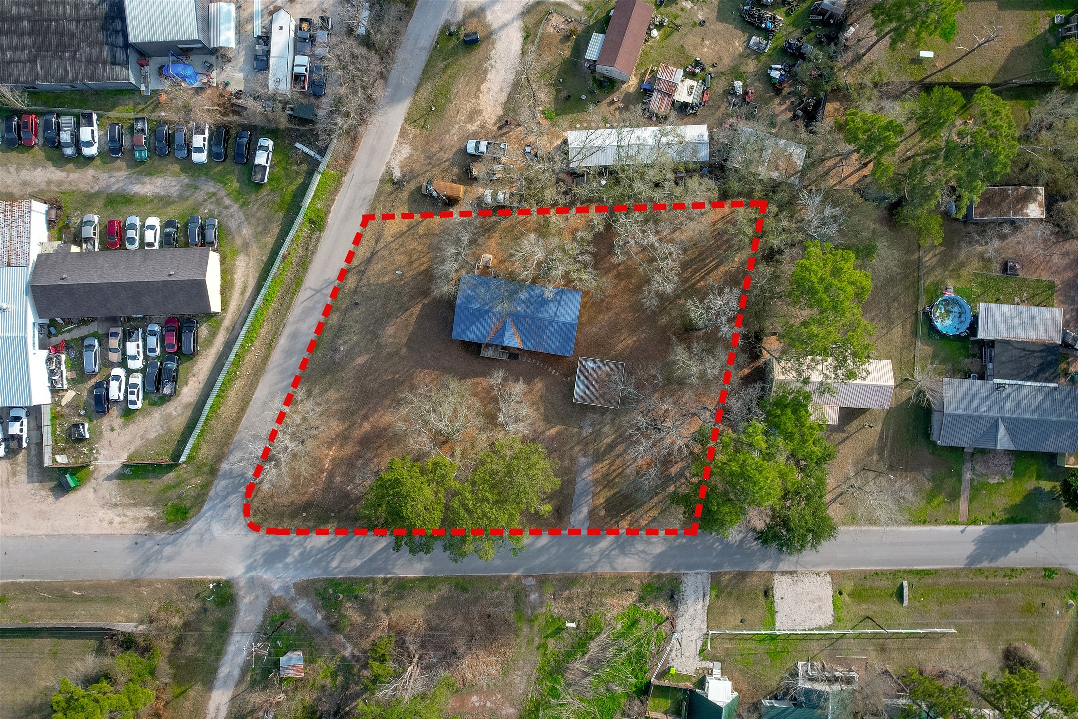 22094 Spear Road Porter, TX 77365 - Photo 40 of 45 This aerial photo shows a property outlined in red, featuring the house with a blue roof, surrounded by trees. It's located on a corner with access to two roads and is adjacent to a developed area with several buildings and parked cars. The lot is spacious, offering potential for development.