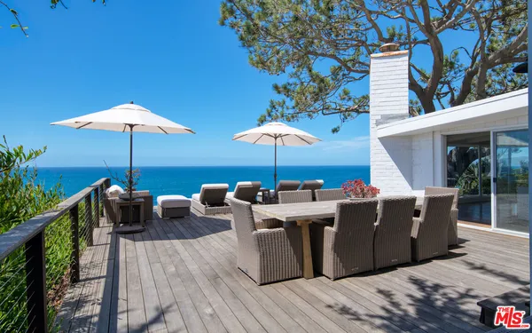 a view of a patio with couches table and chairs under an umbrella with a fire pit