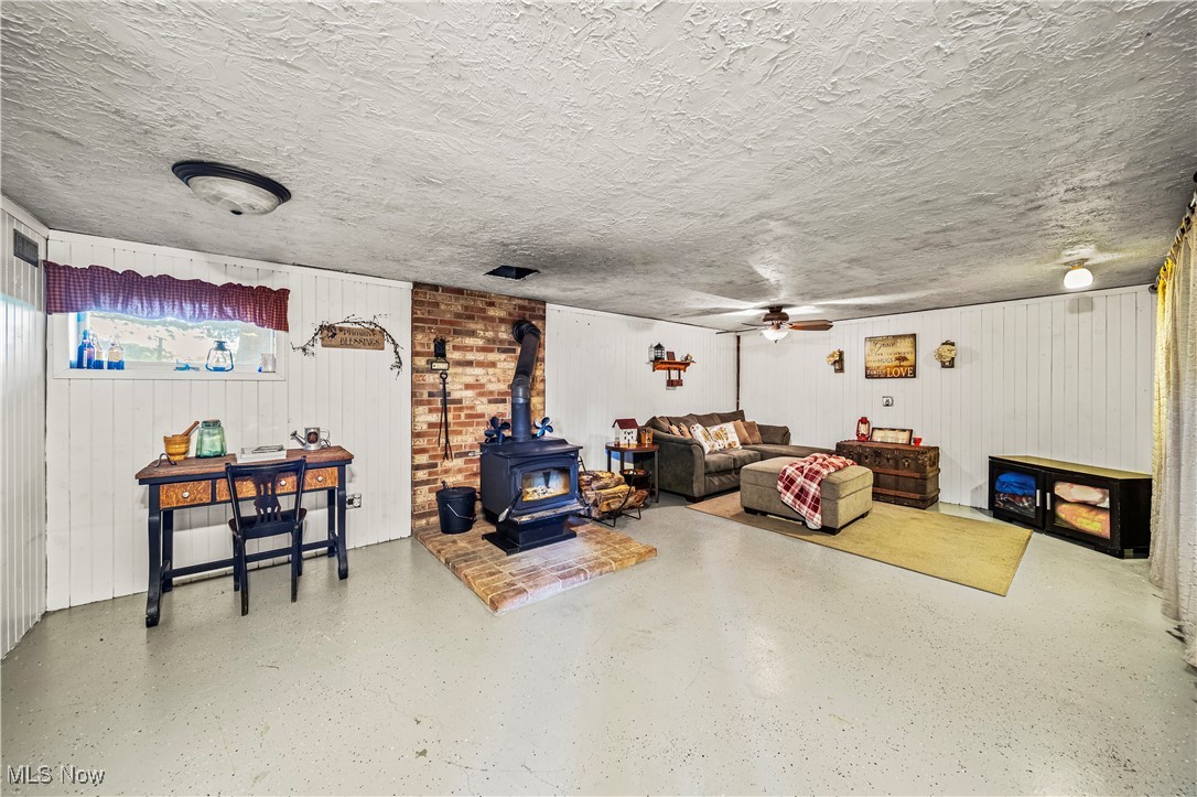 6981 Howard Road Williamsfield, OH 44093 - Photo 28 of 42 Living room featuring a wood stove, wooden walls, ceiling fan, and a textured ceiling