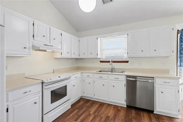 a kitchen with stainless steel appliances granite countertop a sink a stove a refrigerator and white cabinets with wooden floor