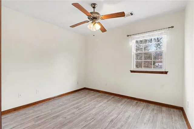 an empty room with wooden floor chandelier fan and windows