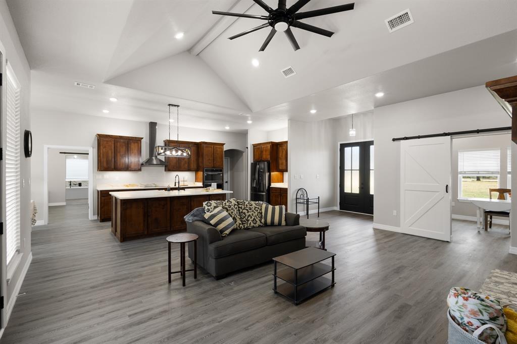 1404 Faulkner Road Sunset, TX 76270 - Photo 13 of 40 Living room featuring a barn door, beamed ceiling, a ceiling fan, dark wood-style floors, and high vaulted ceiling