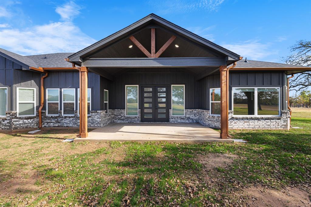 1404 Faulkner Road Sunset, TX 76270 - Photo 35 of 40 Rear view of property with board and batten siding, a patio, a yard, roof with shingles, and stone siding
