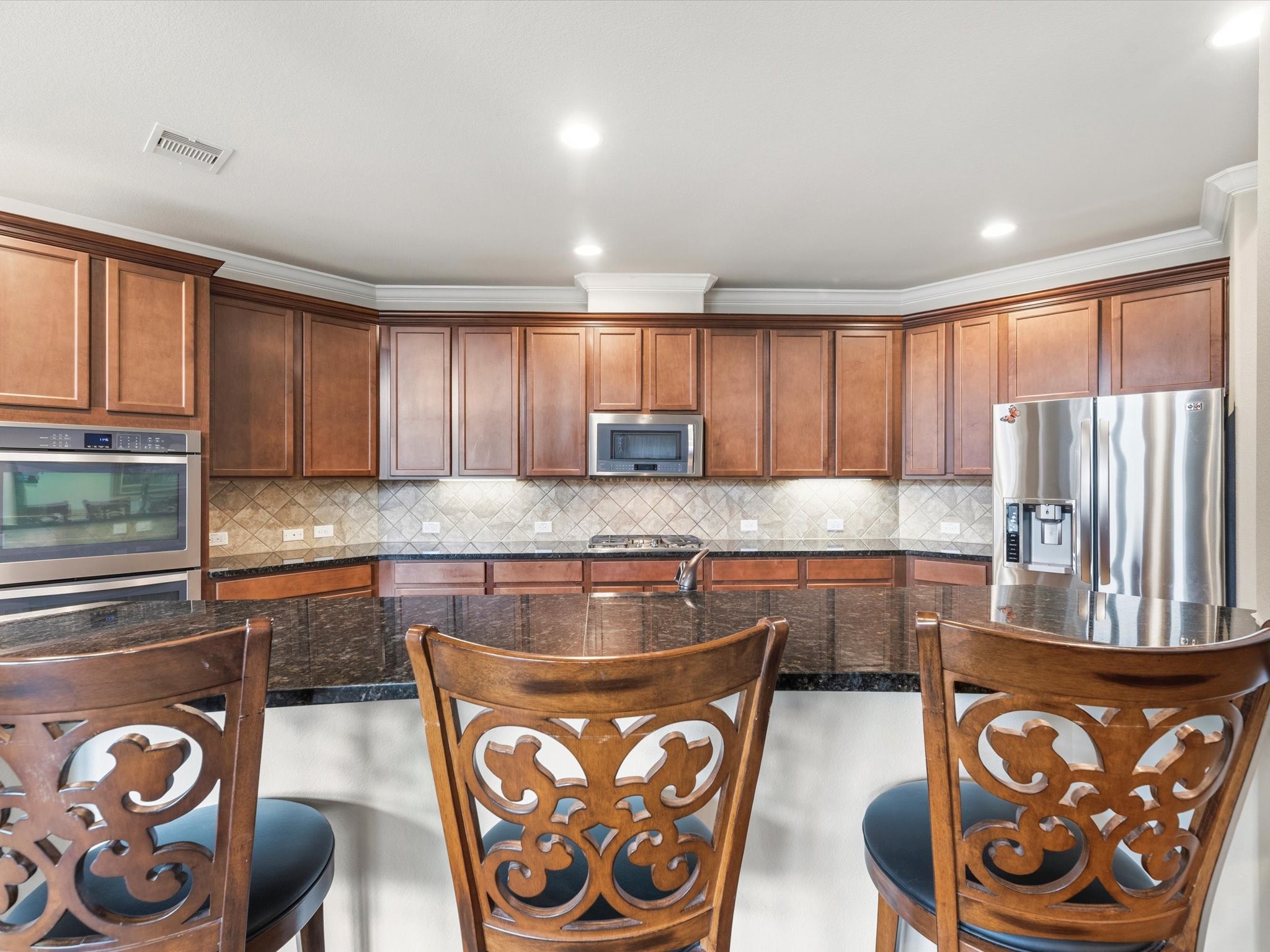 3907 Randle Ridge Court Fulshear, TX 77441 - Photo 10 of 46 Spacious kitchen with elegant wood cabinetry, granite countertops, and stainless steel appliances. Features a large countertop space with bar seating, tiled backsplash, and ample lighting, perfect for entertaining.