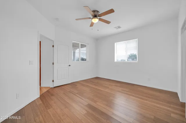 an empty room with wooden floor ceiling fan and window