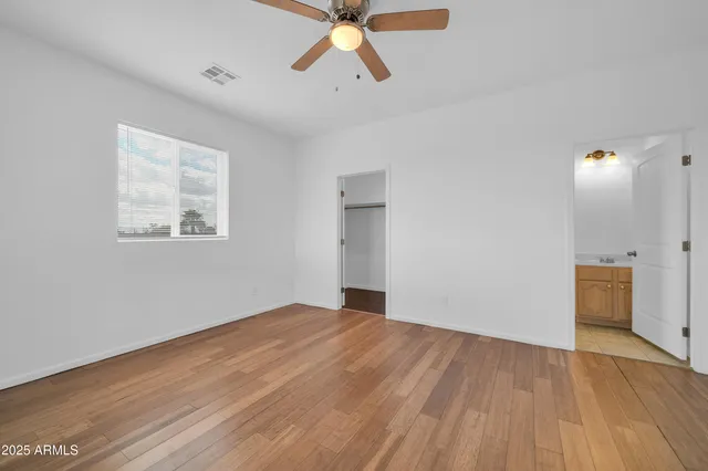 a view of an empty room with wooden floor and a ceiling fan