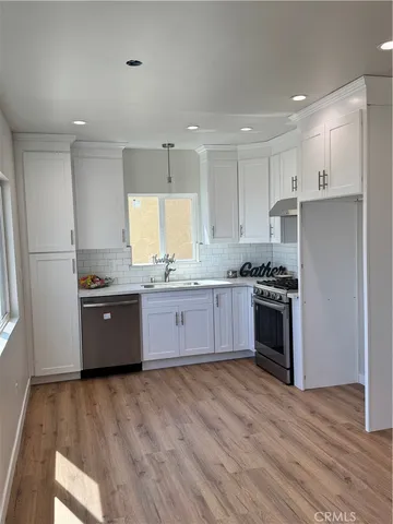 a large kitchen with stainless steel appliances granite countertop a stove a sink dishwasher a refrigerator and white cabinets with wooden floor
