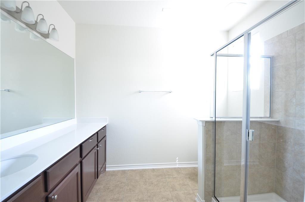 14403 McCoy Loop Austin, TX 78717 - Photo 13 of 29 A well-lit primary bathroom features an elongated vanity with a single basin, a mirror, and a glass-enclosed shower.
