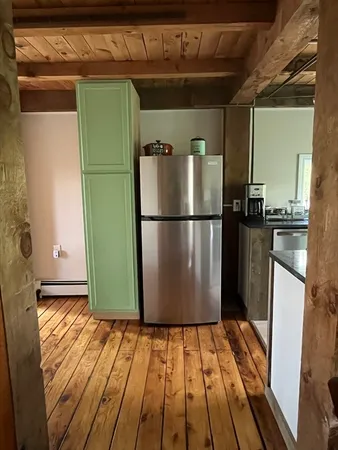 a view of a refrigerator in kitchen and an empty room with wooden floor
