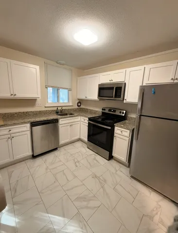 a kitchen with granite countertop a refrigerator sink and white cabinets