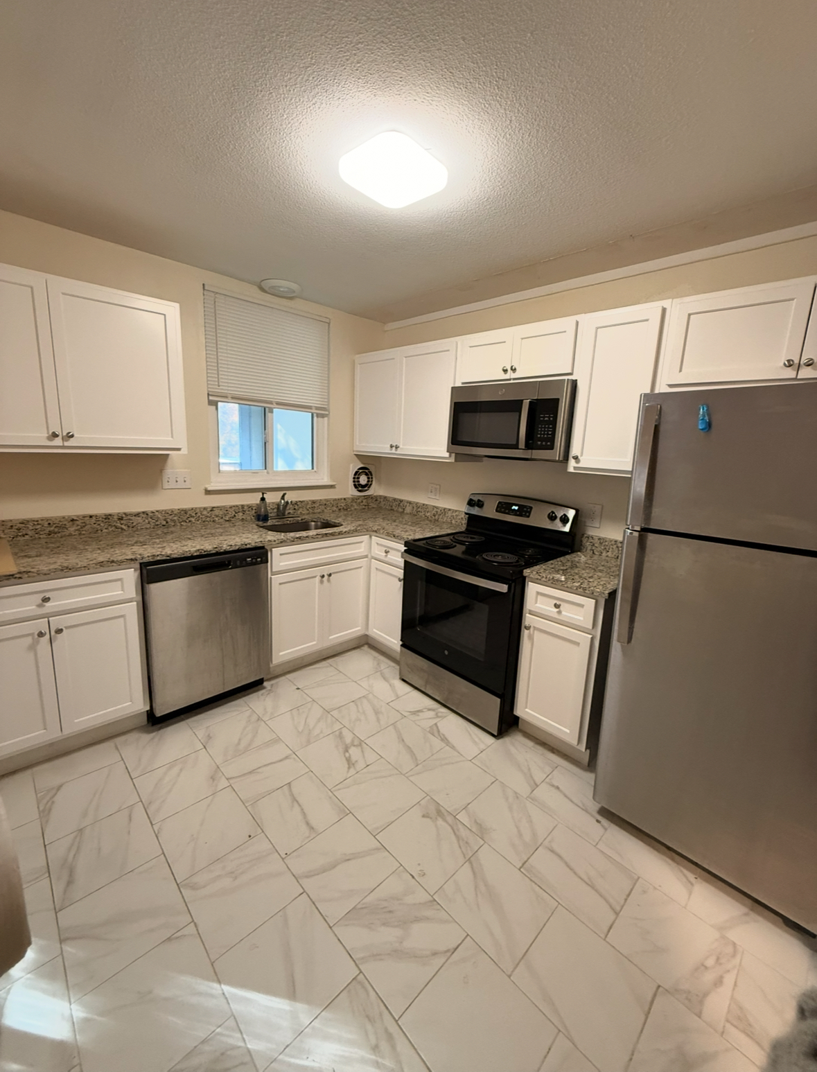 a kitchen with granite countertop a refrigerator sink and white cabinets