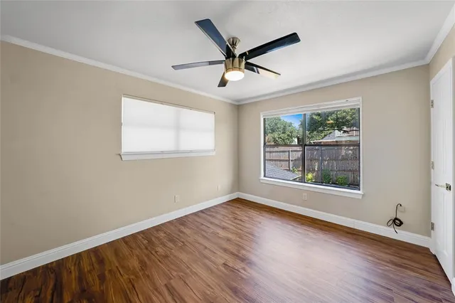 an empty room with wooden floor ceiling fan and windows