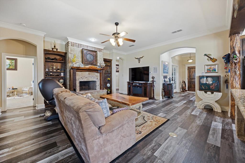 119 George Owens Road Ponder, TX 76259 - Photo 6 of 26 Living area featuring wood-finish flooring, a stone and brick fireplace with an ornate wooden mantel, crown molding, and built-in shelving