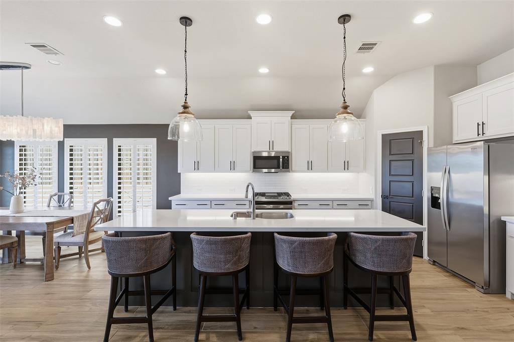 5640 Pradera Road Fort Worth, TX 76126 - Photo 9 of 35 Kitchen island with a light-toned countertop, stainless steel appliances, white cabinetry, wood-finish flooring, and pendant lighting