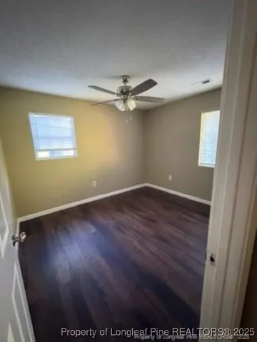 an empty room with wooden floor fan and windows