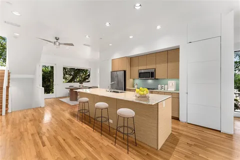 a open kitchen with stainless steel appliances granite countertop a refrigerator a stove top oven a dining table and chairs with wooden floor