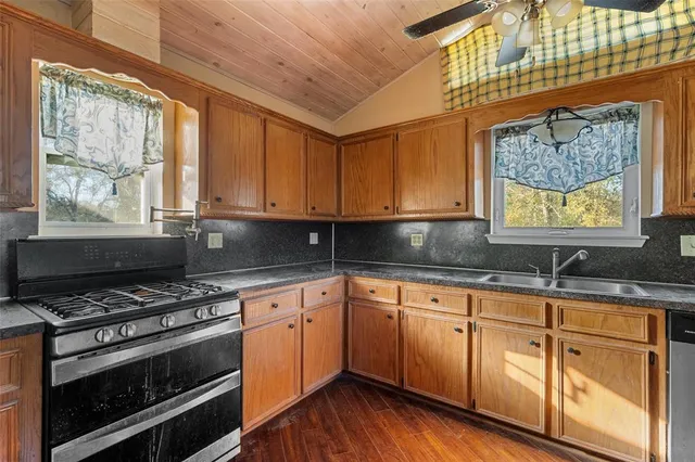 a kitchen with granite countertop a stove a sink and dishwasher wooden cabinets with wooden floor