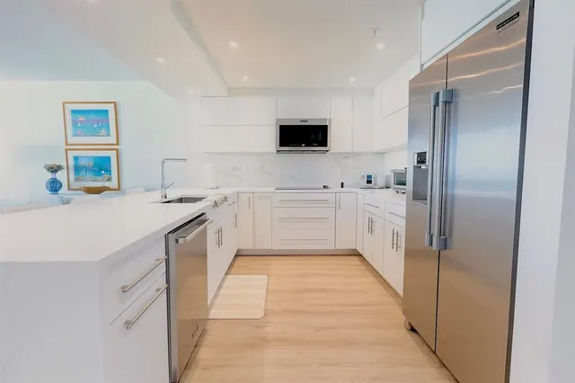 a large white kitchen with a sink and dishwasher a refrigerator with white cabinets